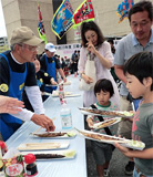 7Zs2時間半並んでも、これも震災復興支援と静かに待つ。焼き立ての香ばしいサンマ手にすると、「おいしそう」と笑顔になる。(撮影:穂高健一、9月23日、東京)